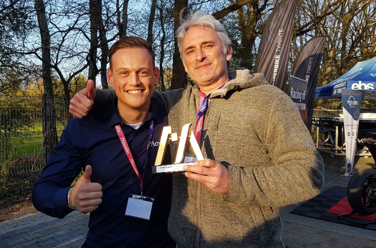 Frank Emrich from scalefit puts his arm around the shoulder of a Movella employee, they show the "thumbs up" gesture and are happy about the award scalefit won as the most effective partner in the field of health and sports.